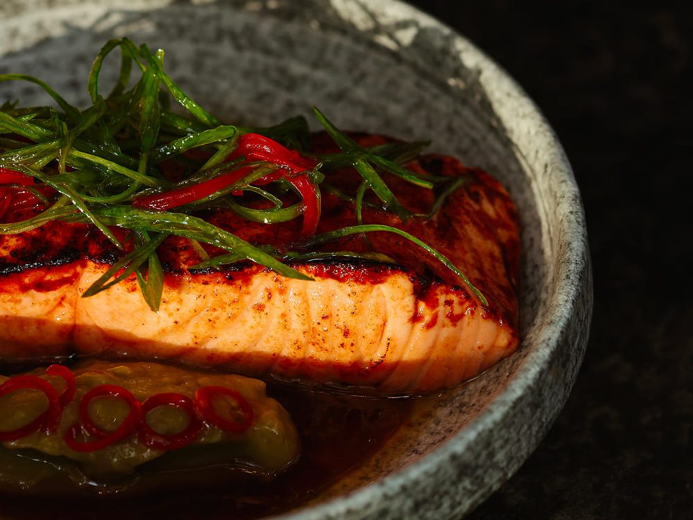 Salmon in a stone bowl under sliced red chilli and spring onion.